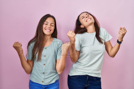 Photo for Young mother and daughter standing over pink background celebrating surprised and amazed for success with arms raised and eyes closed. winner concept. - Royalty Free Image