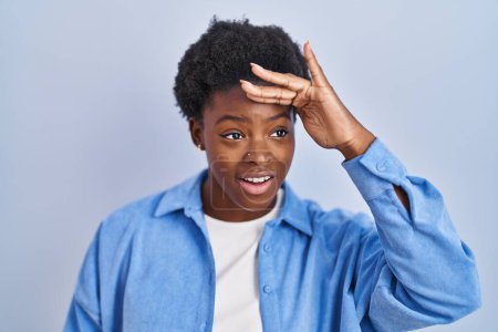 Photo for African american woman standing over blue background very happy and smiling looking far away with hand over head. searching concept. - Royalty Free Image