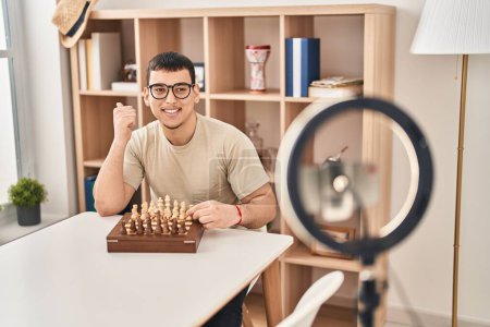 Foto de Joven árabe haciendo tutorial de ajedrez apuntando el pulgar hacia el lado sonriendo feliz con la boca abierta - Imagen libre de derechos