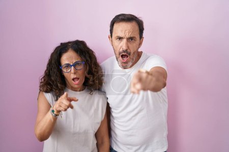 Foto de Mediana edad pareja hispana juntos sobre fondo rosa señalando disgustado y frustrado a la cámara, enojado y furioso con usted - Imagen libre de derechos