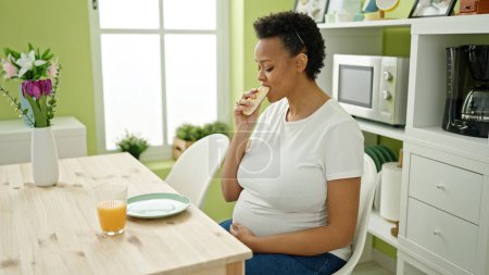 Téléchargez les photos : Jeune femme enceinte petit déjeuner assis sur la table dans la salle à manger - en image libre de droit