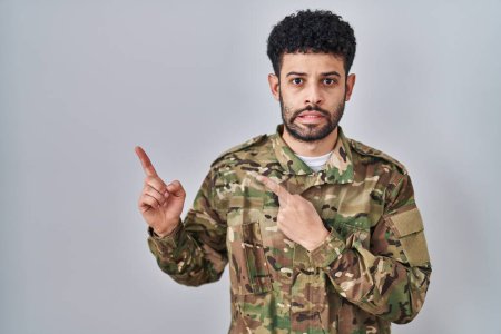Photo for Arab man wearing camouflage army uniform pointing aside worried and nervous with both hands, concerned and surprised expression - Royalty Free Image