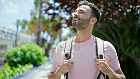 Téléchargez les photos : Jeune homme hispanique touriste portant un sac à dos regardant autour en souriant au parc - en image libre de droit