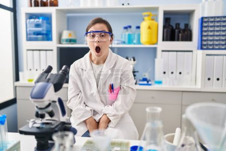 Photo for Hispanic girl with down syndrome working at scientist laboratory afraid and shocked with surprise and amazed expression, fear and excited face. - Royalty Free Image