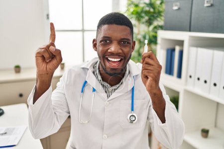 Téléchargez les photos : Un médecin afro-américain tenant des gouttes ophtalmiques souriant avec une idée ou une question pointant du doigt avec un visage heureux, numéro un - en image libre de droit