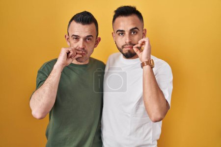 Photo for Homosexual couple standing over yellow background mouth and lips shut as zip with fingers. secret and silent, taboo talking - Royalty Free Image