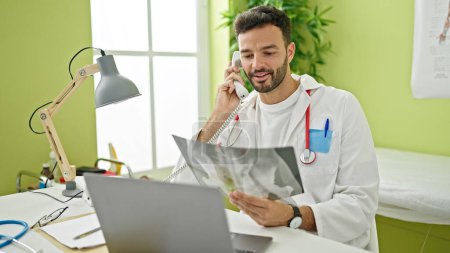 Téléchargez les photos : Jeune homme hispanique médecin parlant au téléphone tenant des rayons X à la clinique - en image libre de droit