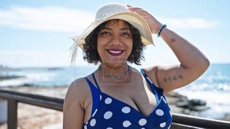 Foto de Joven hermosa mujer latina turista sonriendo confiado usando sombrero de verano en la playa - Imagen libre de derechos