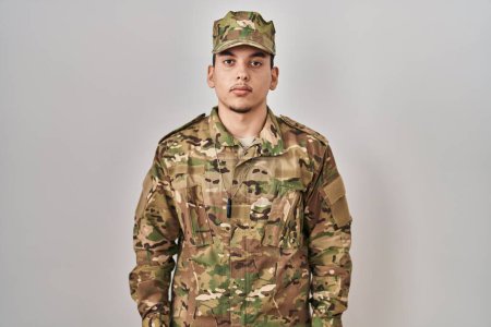 Téléchargez les photos : Jeune homme arabe portant un uniforme de camouflage de l'armée détendue avec une expression sérieuse sur le visage. simple et naturel regardant la caméra. - en image libre de droit