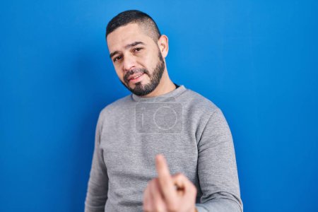 Téléchargez les photos : L'homme hispanique debout sur fond bleu fait signe de venir ici geste avec la main invitant accueillant heureux et souriant - en image libre de droit