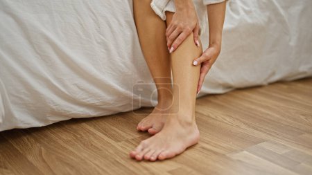 Téléchargez les photos : Jeune femme blonde en peignoir massant la jambe dans la chambre - en image libre de droit