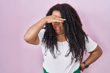 Photo for Plus size hispanic woman standing over pink background smelling something stinky and disgusting, intolerable smell, holding breath with fingers on nose. bad smell - Royalty Free Image