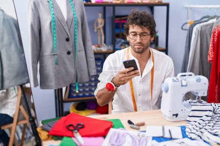 Téléchargez les photos : Young hispanic man tailor using smartphone at clothing factory - en image libre de droit