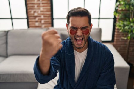 Foto de Joven hombre hispano con barba con ojos de belleza parche molesto y frustrado gritando con ira, gritando loco de ira y la mano levantada - Imagen libre de derechos