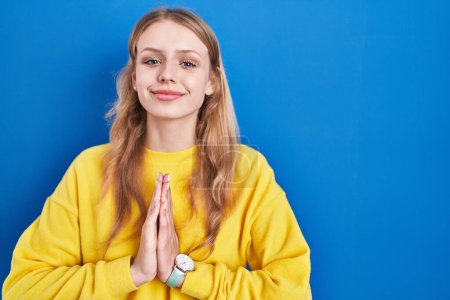 Photo for Young caucasian woman standing over blue background praying with hands together asking for forgiveness smiling confident. - Royalty Free Image