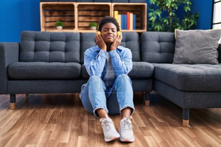 Photo for African american woman listening to music sitting on floor at home - Royalty Free Image