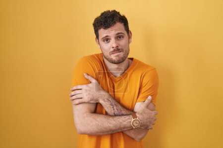 Photo for Young hispanic man standing over yellow background shaking and freezing for winter cold with sad and shock expression on face - Royalty Free Image