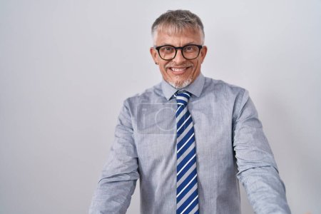 Photo for Hispanic business man with grey hair wearing glasses smiling cheerful with open arms as friendly welcome, positive and confident greetings - Royalty Free Image