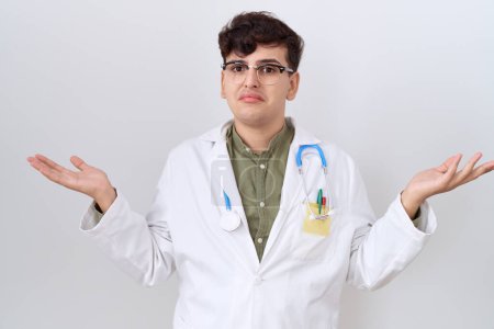 Photo for Young non binary man wearing doctor uniform and stethoscope clueless and confused expression with arms and hands raised. doubt concept. - Royalty Free Image
