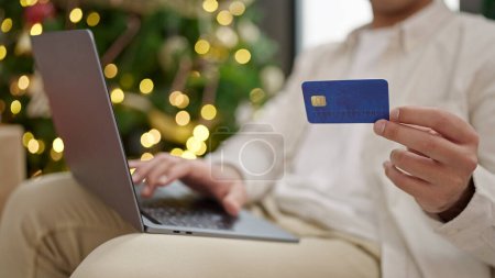 Photo for Young hispanic man shopping with laptop and credit card celebrating christmas at home - Royalty Free Image