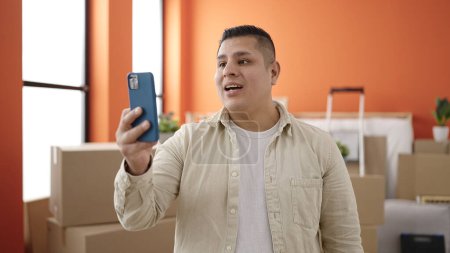 Téléchargez les photos : Jeune homme hispanique ayant appel vidéo debout à la nouvelle maison - en image libre de droit