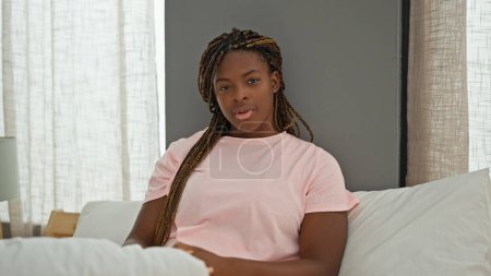 Foto de Mujer afroamericana sentada en la cama con cara seria en el dormitorio - Imagen libre de derechos