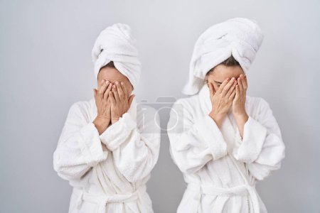 Foto de Mujer e hija de mediana edad con albornoz blanco y toalla con expresión triste que cubre la cara con las manos mientras llora. concepto de depresión. - Imagen libre de derechos