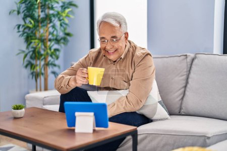 Foto de Hombre mayor bebiendo café viendo touchpad en casa - Imagen libre de derechos