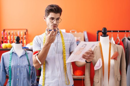 Téléchargez les photos : Young hispanic man tailor talking on smartphone looking clothing design at atelier - en image libre de droit