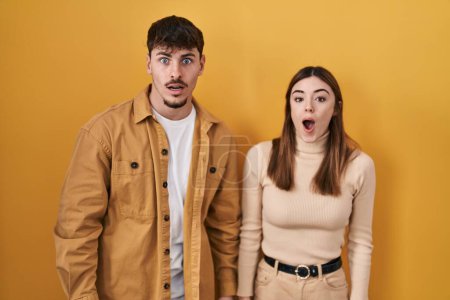 Photo for Young hispanic couple standing over yellow background afraid and shocked with surprise and amazed expression, fear and excited face. - Royalty Free Image