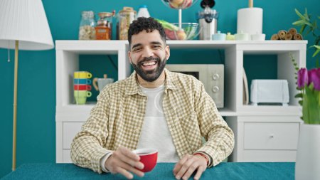 Téléchargez les photos : Jeune homme hispanique buvant du café assis sur la table de la salle à manger - en image libre de droit