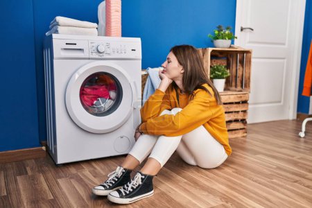 Téléchargez les photos : Young blonde woman sitting on floor waiting for washing machine at laundry room - en image libre de droit