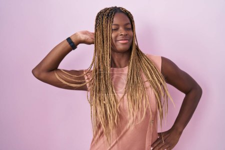 Foto de Mujer afroamericana con cabello trenzado de pie sobre fondo rosa que se extiende hacia atrás, cansado y relajado, soñoliento y bostezando por la mañana temprano - Imagen libre de derechos