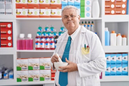 Téléchargez les photos : Moyen âge homme cheveux gris pharmacien souriant confiant faire mélange à la pharmacie - en image libre de droit