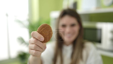 Photo for Young beautiful hispanic woman holding cookie sitting on table at dinning room - Royalty Free Image