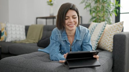 Foto de Mujer caucásica joven usando touchpad acostado en el sofá en casa - Imagen libre de derechos