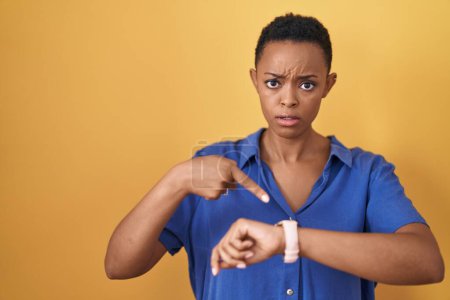 Téléchargez les photos : Femme afro-américaine debout sur fond jaune pressé pointant vers regarder le temps, l'impatience, bouleversé et en colère pour retard de délai - en image libre de droit