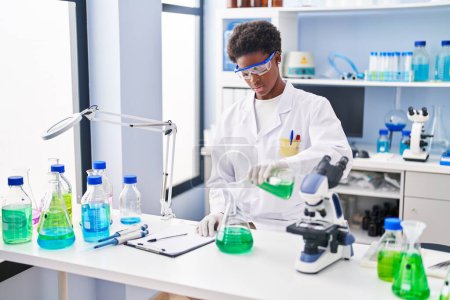 Téléchargez les photos : Femme afro-américaine portant un uniforme scientifique mesurant le liquide au laboratoire - en image libre de droit