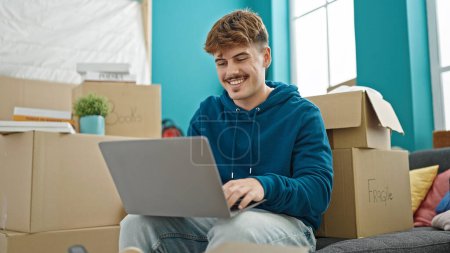 Photo for Young hispanic man using laptop sitting on sofa at new home - Royalty Free Image