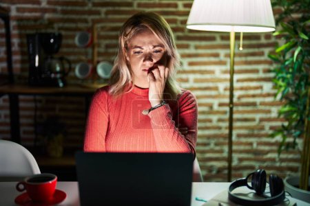 Photo for Blonde woman using laptop at night at home looking stressed and nervous with hands on mouth biting nails. anxiety problem. - Royalty Free Image