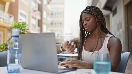 Téléchargez les photos : Femme afro-américaine à l'aide d'un ordinateur portable regarder à la terrasse du café - en image libre de droit