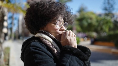 Téléchargez les photos : Jeune femme afro-américaine portant une écharpe pour le froid frotter les mains ensemble au parc - en image libre de droit