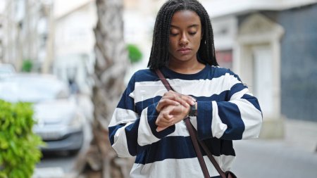 Téléchargez les photos : Femme afro-américaine regardant la montre en attente avec une expression sérieuse dans la rue - en image libre de droit