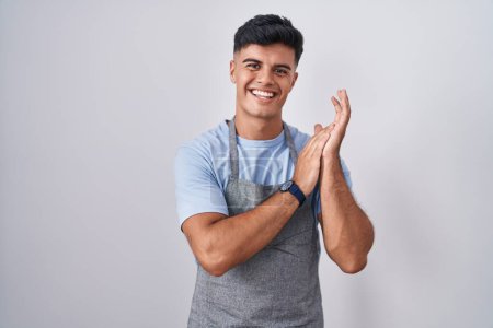 Photo for Hispanic young man wearing apron over white background clapping and applauding happy and joyful, smiling proud hands together - Royalty Free Image