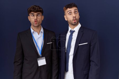 Foto de Dos hombres de negocios hispanos vestidos con ropa de negocios haciendo cara de pez con labios, gesto loco y cómico. expresión divertida. - Imagen libre de derechos