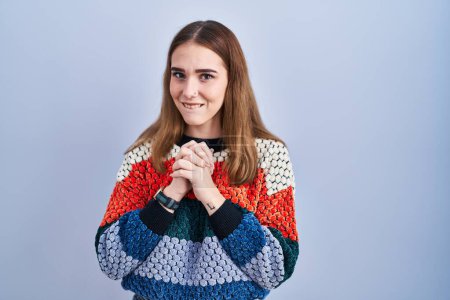 Photo for Young hispanic girl standing over blue background laughing nervous and excited with hands on chin looking to the side - Royalty Free Image
