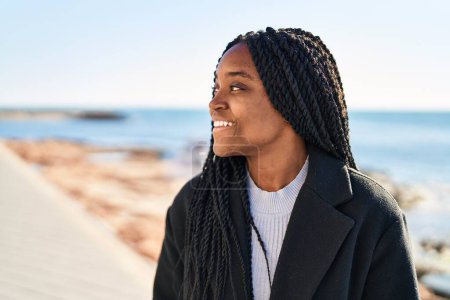 Téléchargez les photos : Afro-américaine femme souriant confiant regardant vers le côté à bord de la mer - en image libre de droit