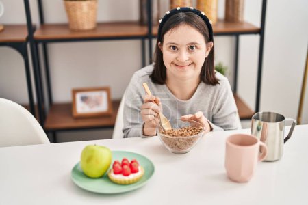 Foto de Mujer joven con síndrome de Down sonriendo confiada desayunando en casa - Imagen libre de derechos