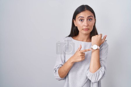 Photo for Young hispanic woman standing over white background in hurry pointing to watch time, impatience, looking at the camera with relaxed expression - Royalty Free Image