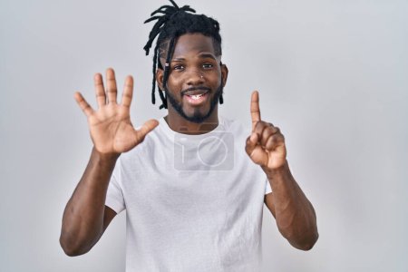 Téléchargez les photos : Homme africain avec dreadlocks portant t-shirt décontracté sur fond blanc montrant et pointant vers le haut avec les doigts numéro six tout en souriant confiant et heureux. - en image libre de droit